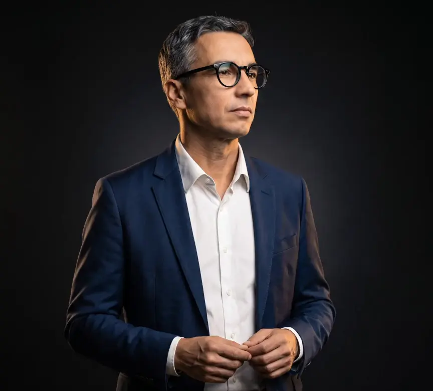 Dr. Daniel Minutti em pé, de terno, num ambiente de luz baixa